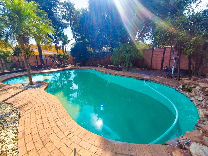 A private swimming pool area featuring brick paving, a rockery feature, and a surrounding boundary wall in a landscaped garden setting.