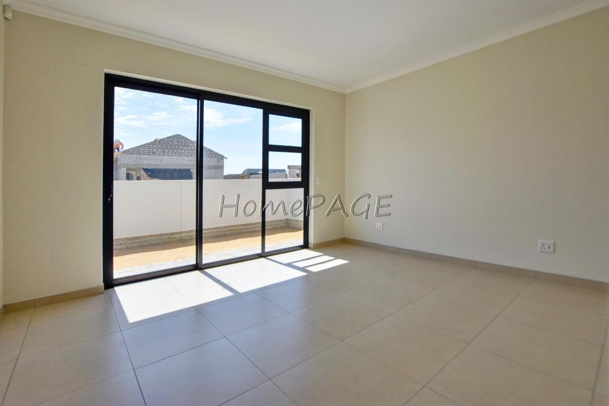 A bright, empty bedroom featuring neutral tiled flooring and large black-framed sliding glass doors that open onto an outdoor patio area.