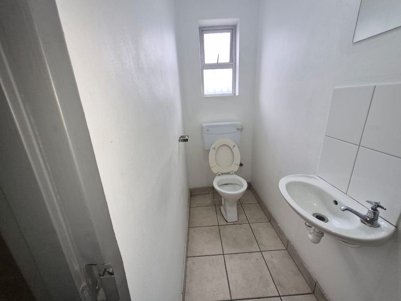 A compact, functional bathroom featuring a wall-mounted basin with tiled splashback, a standard toilet, and tiled flooring.