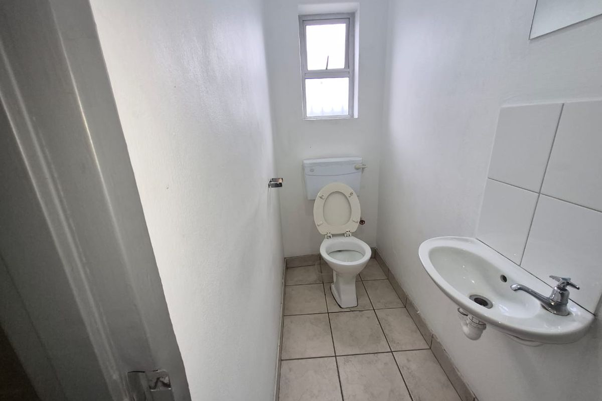 A compact, functional bathroom featuring a wall-mounted basin with tiled splashback, a standard toilet, and tiled flooring.