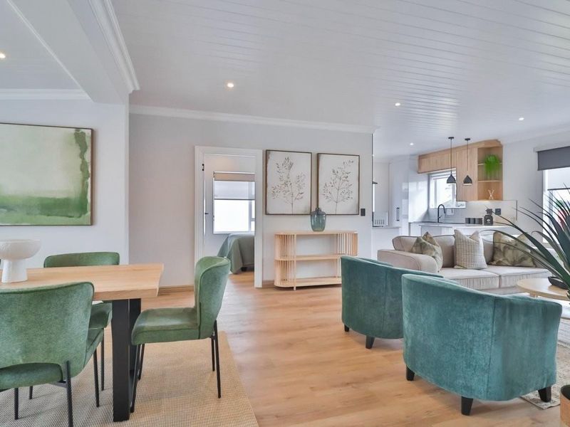 A bright open-plan living and dining area featuring timber flooring, a tongue and groove ceiling, and a modern kitchen with integrated cabinetry.