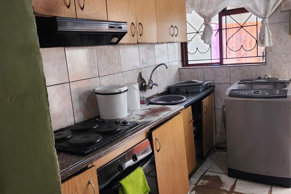 A functional kitchen featuring built-in cabinetry, an electric hob, oven, and tiled finishes, requiring some maintenance and cosmetic updates.