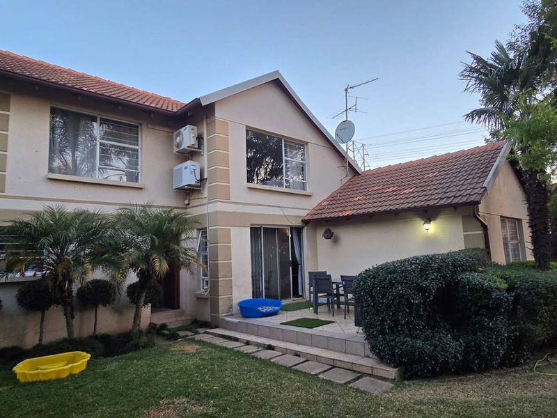 Rear view of the townhouse featuring a tiled roof, a paved patio area, a balcony, and established garden landscaping.