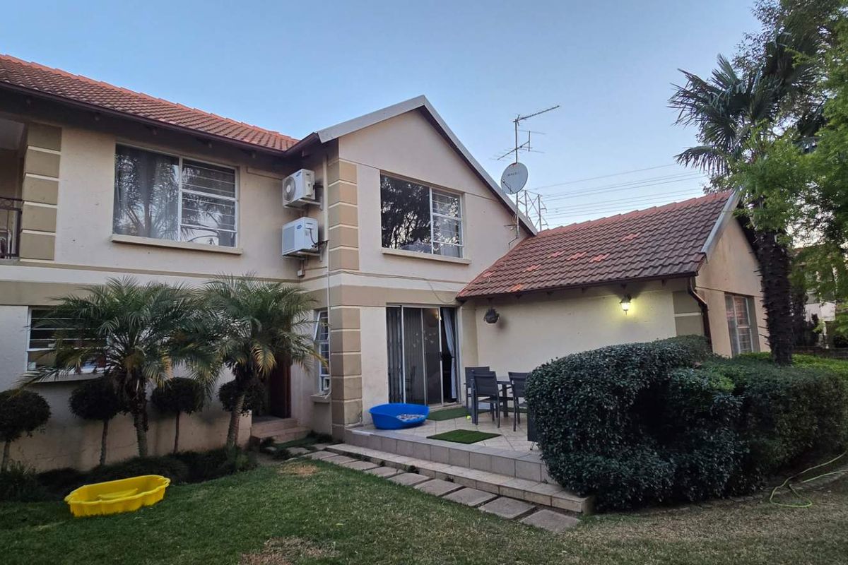 Rear view of the townhouse featuring a tiled roof, a paved patio area, a balcony, and established garden landscaping.