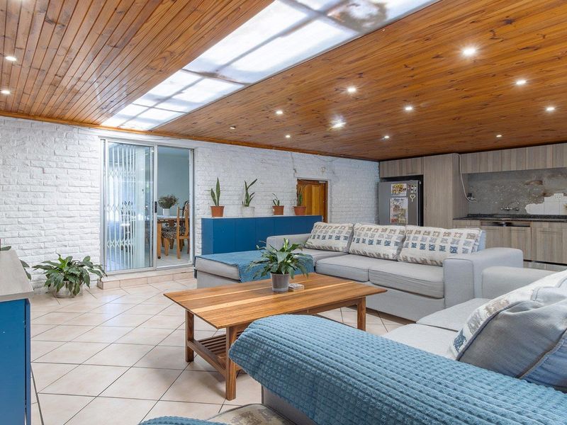 Spacious open-plan living area featuring a timber-clad ceiling with skylight, tiled floors, and an integrated kitchen with stone countertops and ample cabinetry.