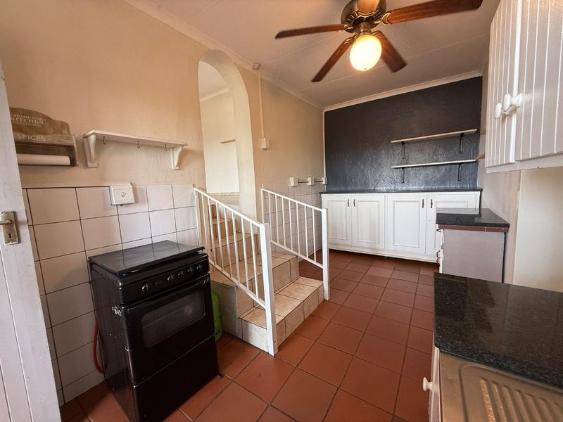 A functional kitchen featuring tiled flooring, granite countertops, built-in cabinetry, and a freestanding stove, with an integrated staircase leading to an adjacent level.