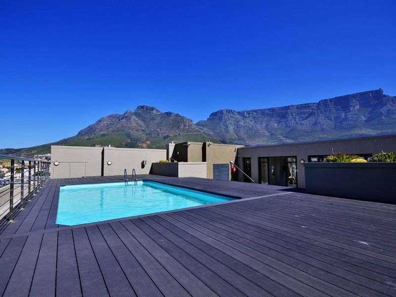 A rooftop swimming pool area featuring modern composite decking, stainless steel railings, and panoramic mountain views.