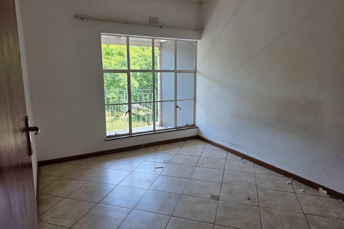 An empty bedroom featuring large grid-style windows, tiled flooring, and access to an outdoor balcony area.