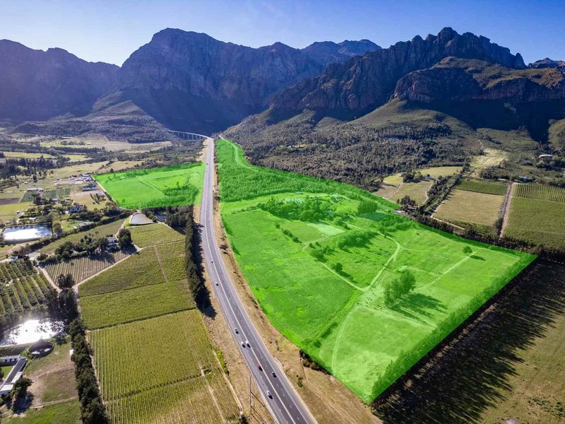 Aerial view of a large farm property highlighted in green, featuring expansive agricultural land situated against a scenic mountain backdrop with highway access.