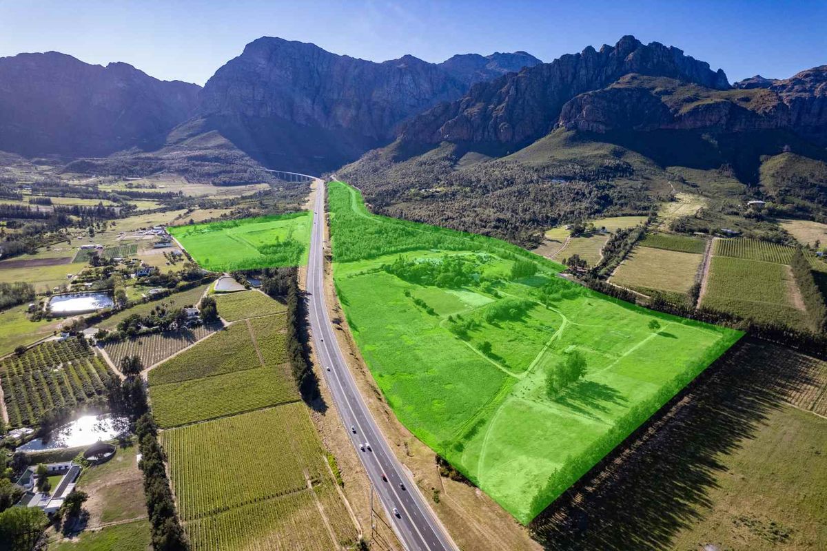 Aerial view of a large farm property highlighted in green, featuring expansive agricultural land situated against a scenic mountain backdrop with highway access.