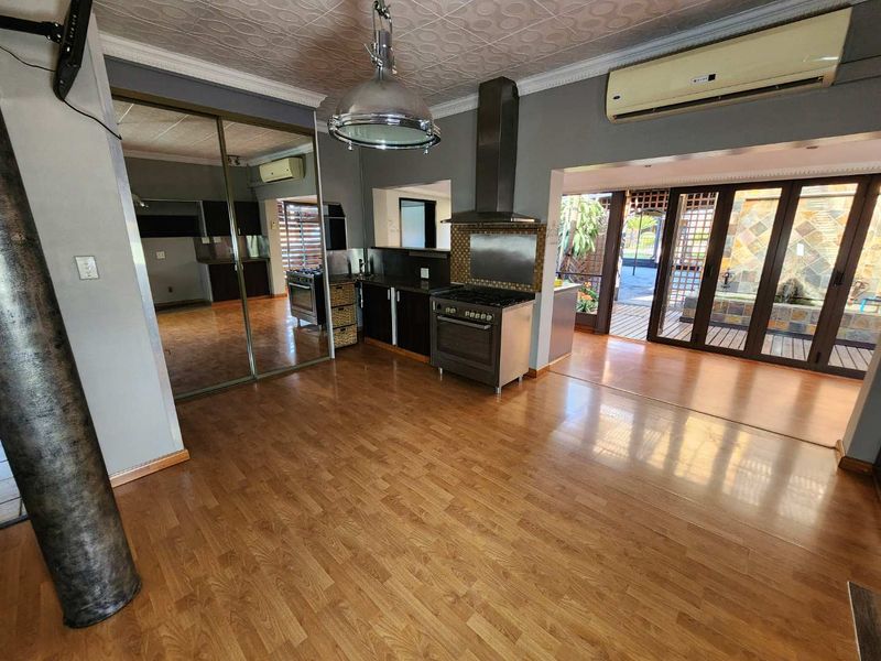 Spacious open-plan living and kitchen area featuring laminate flooring, built-in cabinetry, gas stove, and direct access to an outdoor patio through glass doors.