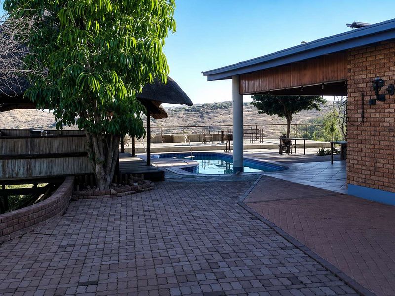 Outdoor entertainment area featuring a swimming pool, thatched gazebo, and spacious paved patio with scenic landscape views.