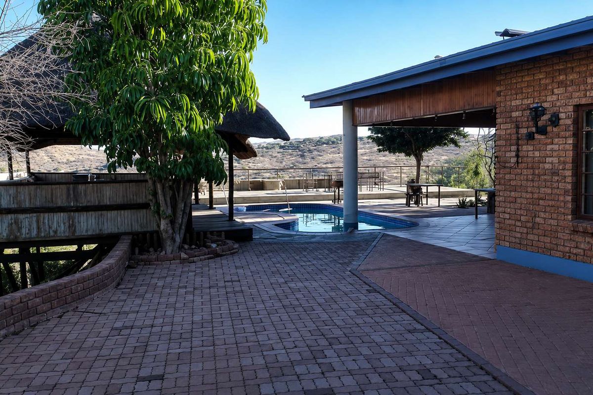 Outdoor entertainment area featuring a swimming pool, thatched gazebo, and spacious paved patio with scenic landscape views.