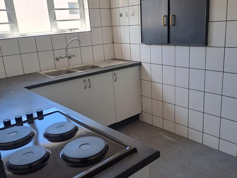 A functional kitchen featuring a built-in electric hob, double sink with mixer tap, and tiled wall finishes with ample storage cabinetry.