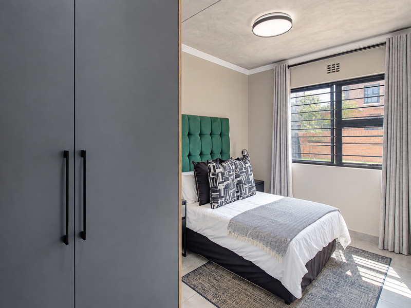 A well-maintained bedroom featuring a built-in wardrobe, tiled flooring, and a window fitted with security bars.