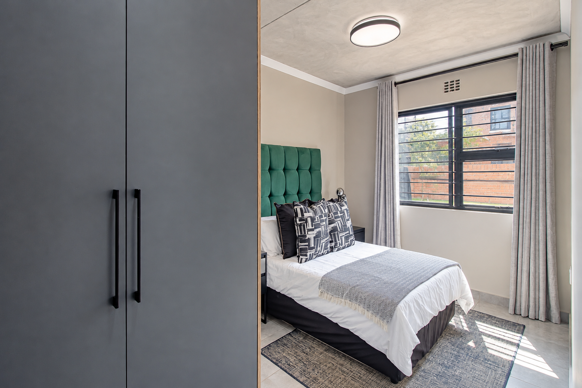 A well-maintained bedroom featuring a built-in wardrobe, tiled flooring, and a window fitted with security bars.