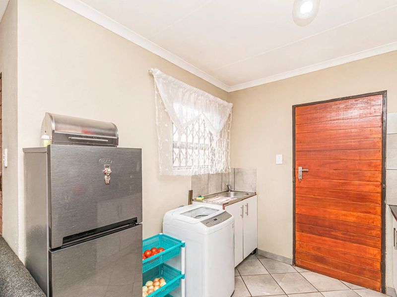 A functional laundry area featuring tiled flooring, a built-in sink with splashback, and cabinetry, providing a practical space for household utility tasks.
