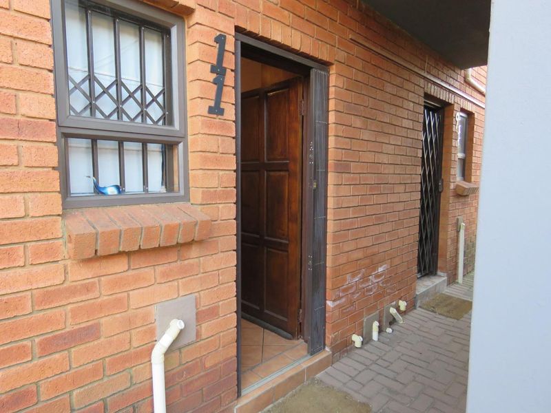 Exterior view of an apartment entrance featuring a brick facade, security gate, and timber door with paved walkway access.