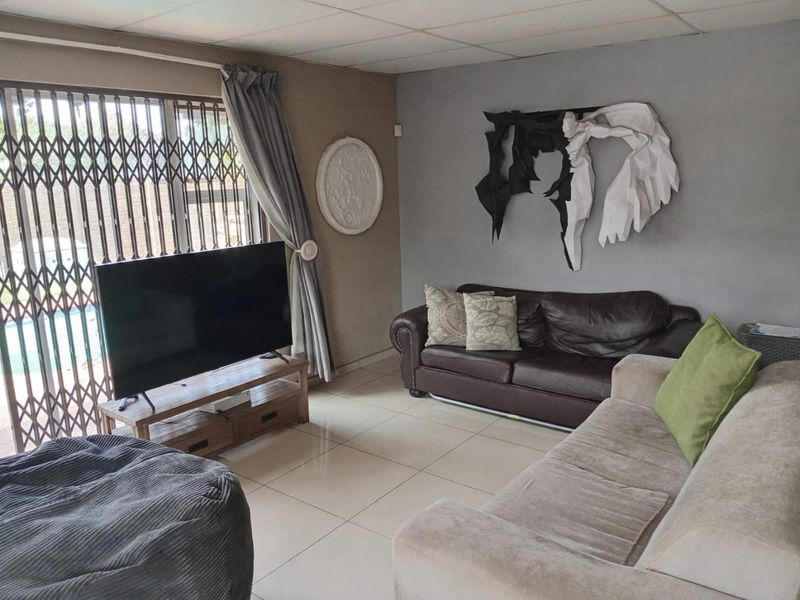 A living room featuring tiled flooring, a drop ceiling, and a sliding door with a security gate leading to the exterior.