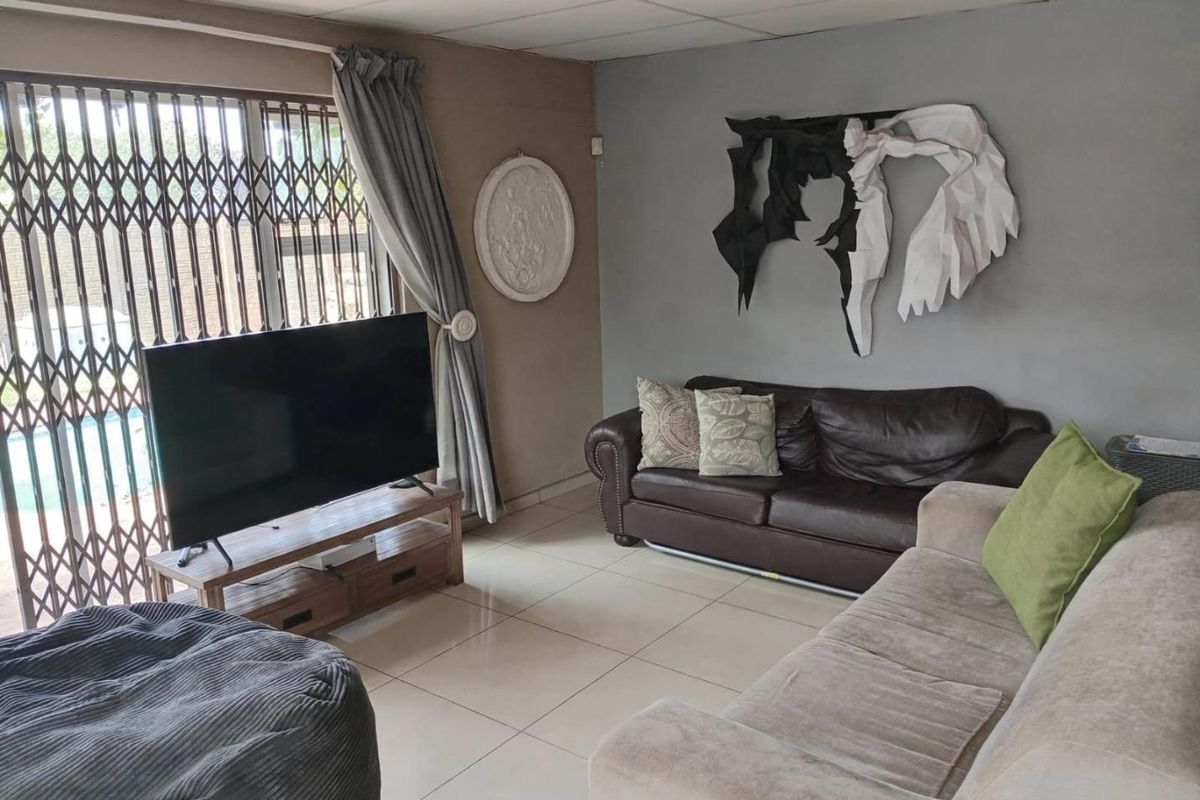 A living room featuring tiled flooring, a drop ceiling, and a sliding door with a security gate leading to the exterior.