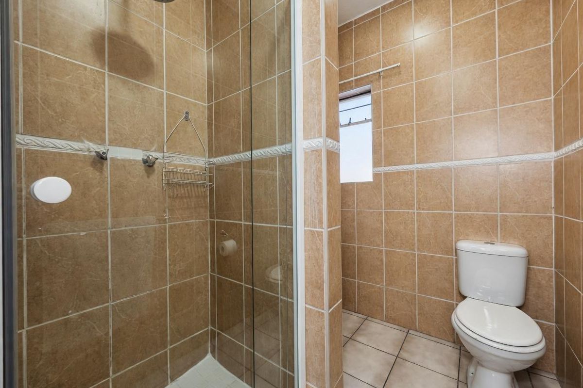 A functional bathroom featuring a glass-enclosed shower with a rainfall showerhead and a standard white toilet, finished with neutral wall and floor tiling.