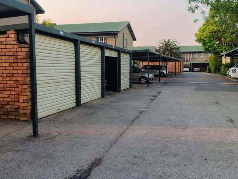 Exterior view of a residential apartment complex featuring a row of individual lock-up garages and covered carport parking bays.