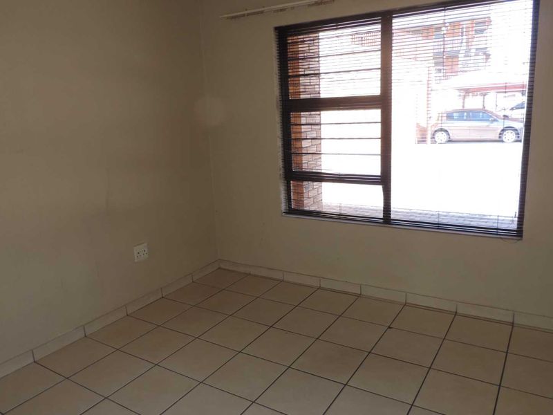 An empty bedroom featuring tiled flooring and a large window with a curtain rail, providing a blank canvas for potential interior design updates.