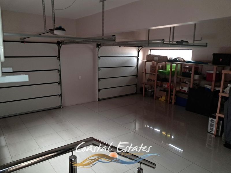Spacious double garage featuring tiled flooring, automated garage doors, and a modern stainless steel balustrade.