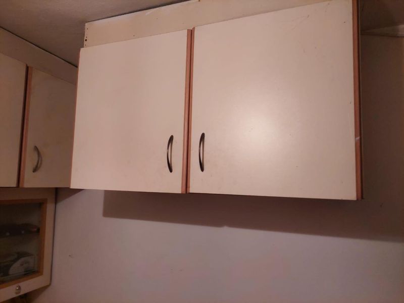 Close-up view of dated wall-mounted kitchen cabinetry showing signs of wear and incomplete installation against the ceiling.
