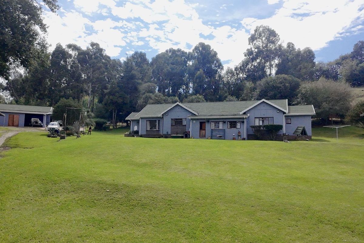 A spacious single-story residence featuring a tiled roof, set on a large, expansive lawn with a detached garage and mature surrounding trees.