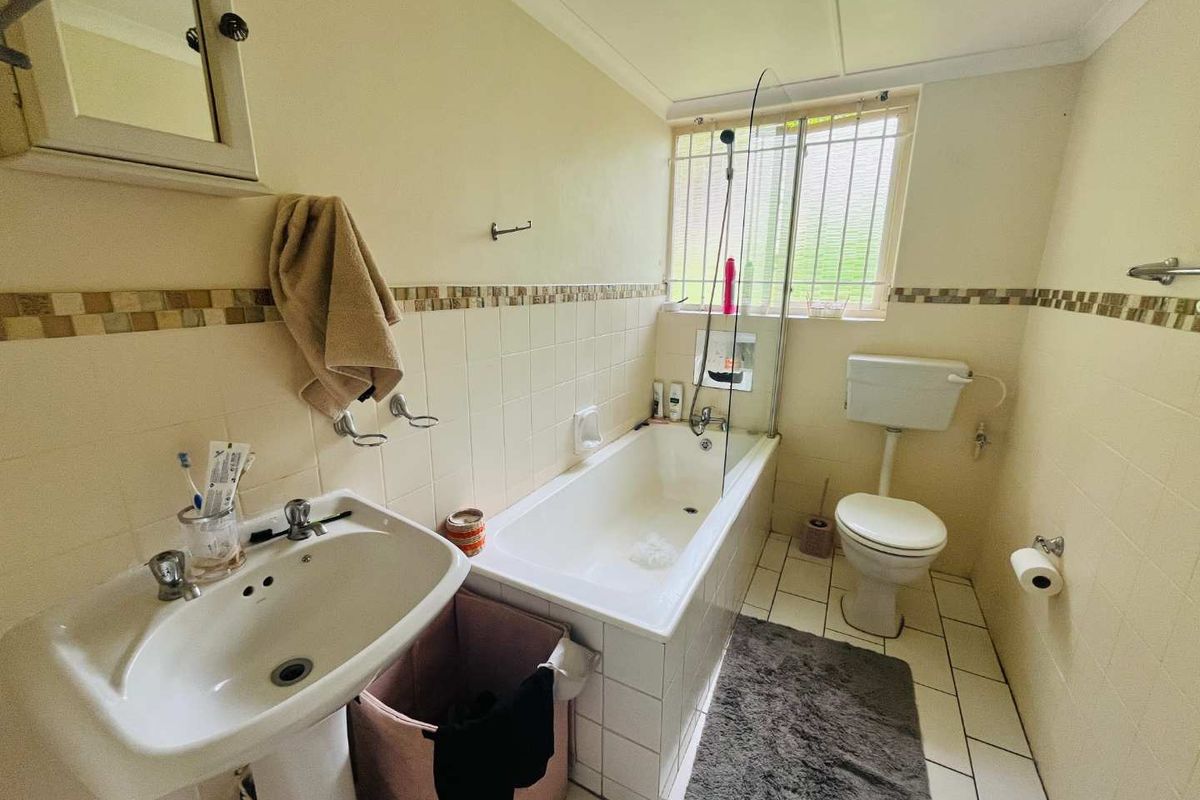 A functional bathroom featuring a pedestal basin, a bathtub with a glass shower screen, and a standard toilet with a high-level cistern.