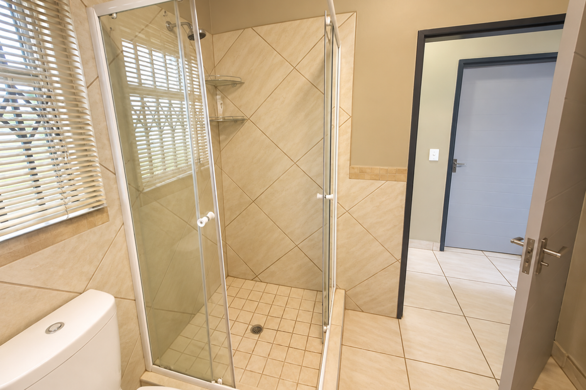 A clean and well-maintained bathroom featuring a glass-enclosed shower, neutral wall and floor tiling, and a modern toilet.