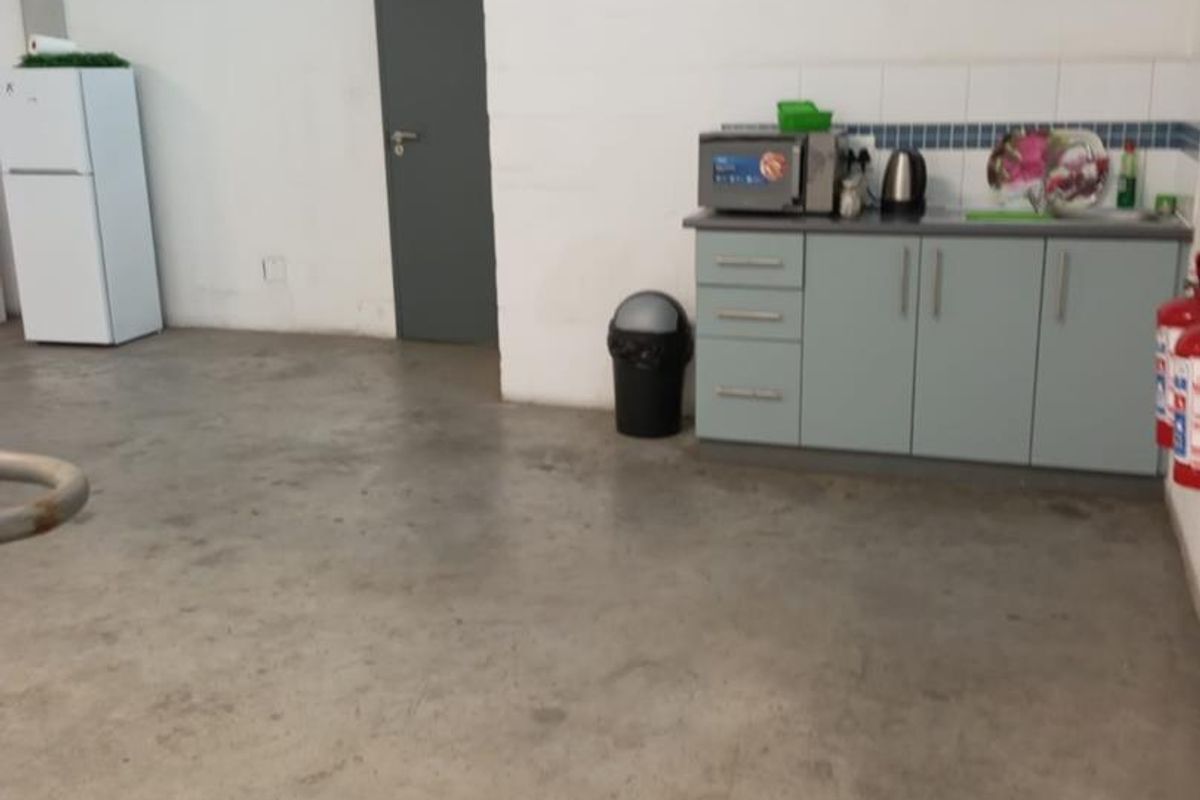 A functional industrial kitchenette area featuring built-in cabinetry, concrete flooring, and essential safety equipment within a warehouse-style space.