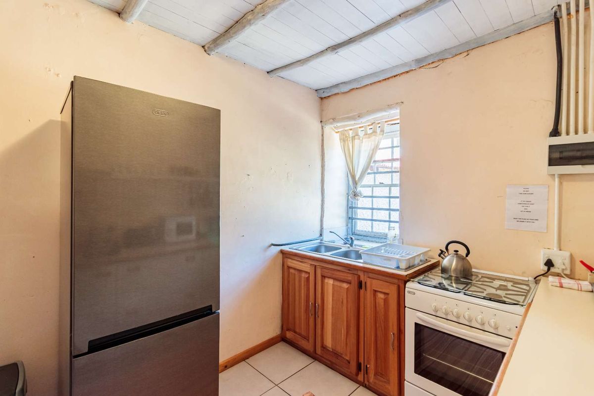 Compact kitchen featuring wooden cabinetry, a double sink, freestanding stove, and exposed beam ceiling, requiring cosmetic updates to improve the overall finish.