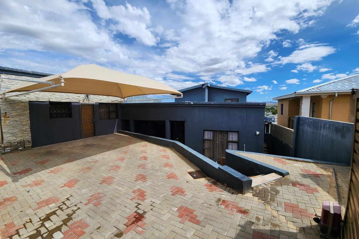 A paved outdoor courtyard area featuring a shade sail, retaining walls, and access to the main building structure.