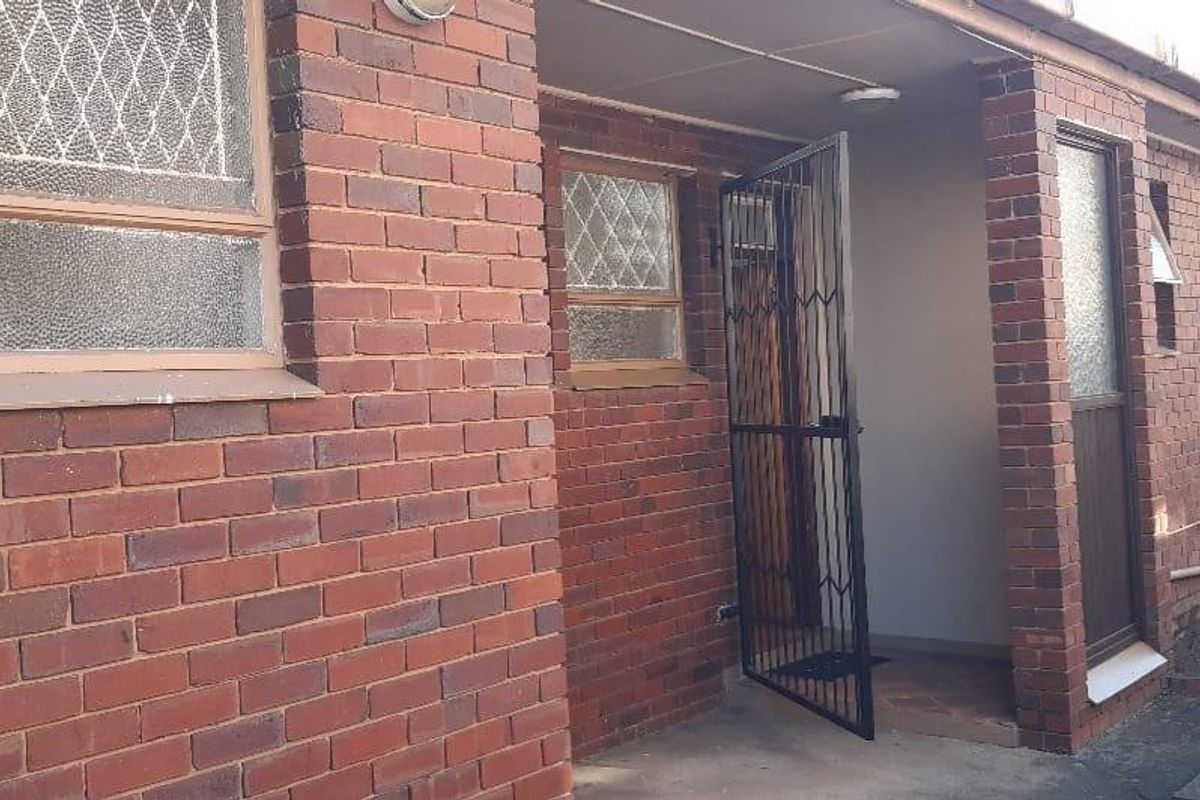 Rear exterior view of an apartment building featuring face brick construction, security gates, and concrete walkways.