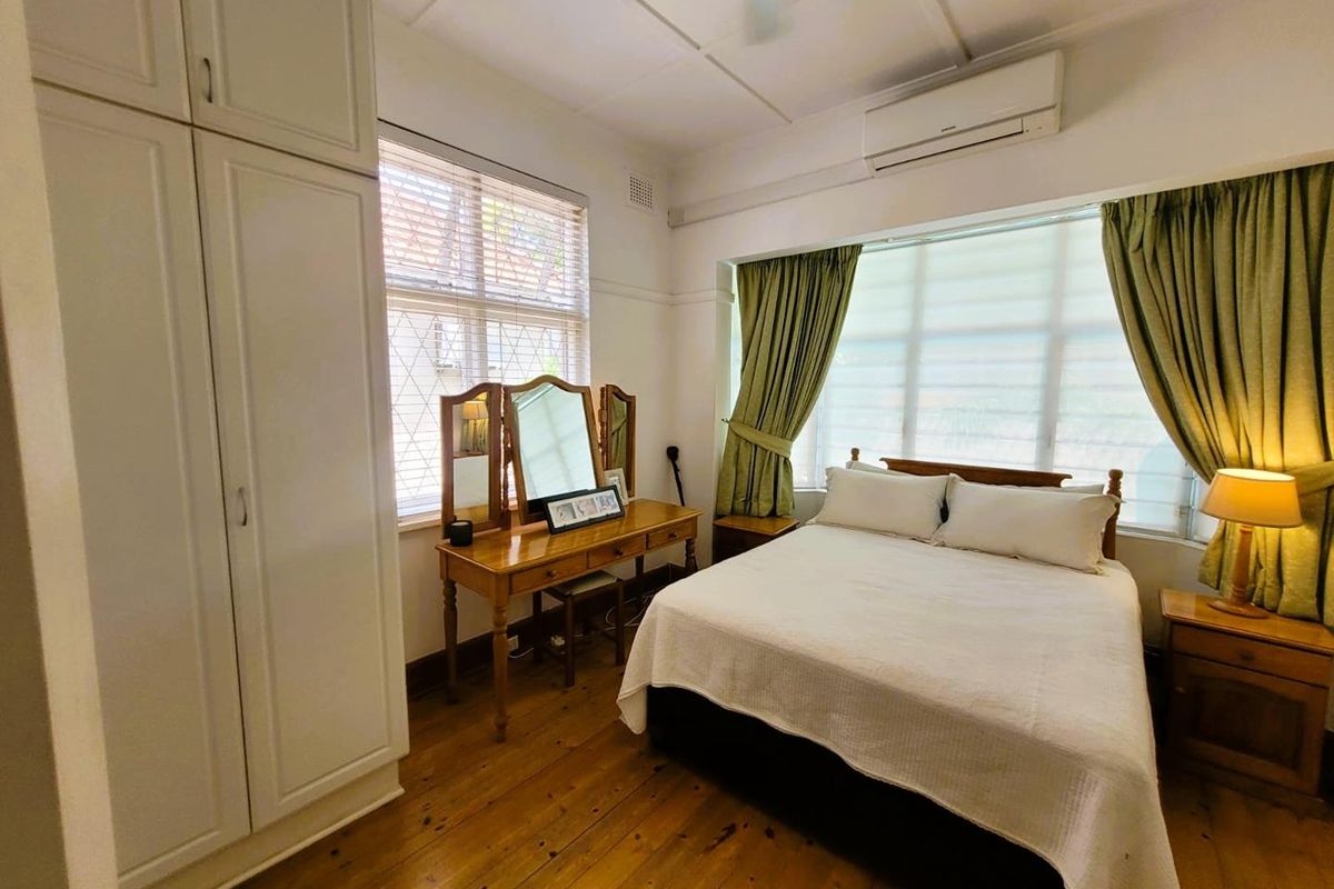 A well-lit bedroom featuring polished timber flooring, built-in cabinetry, and a wall-mounted air conditioning unit.
