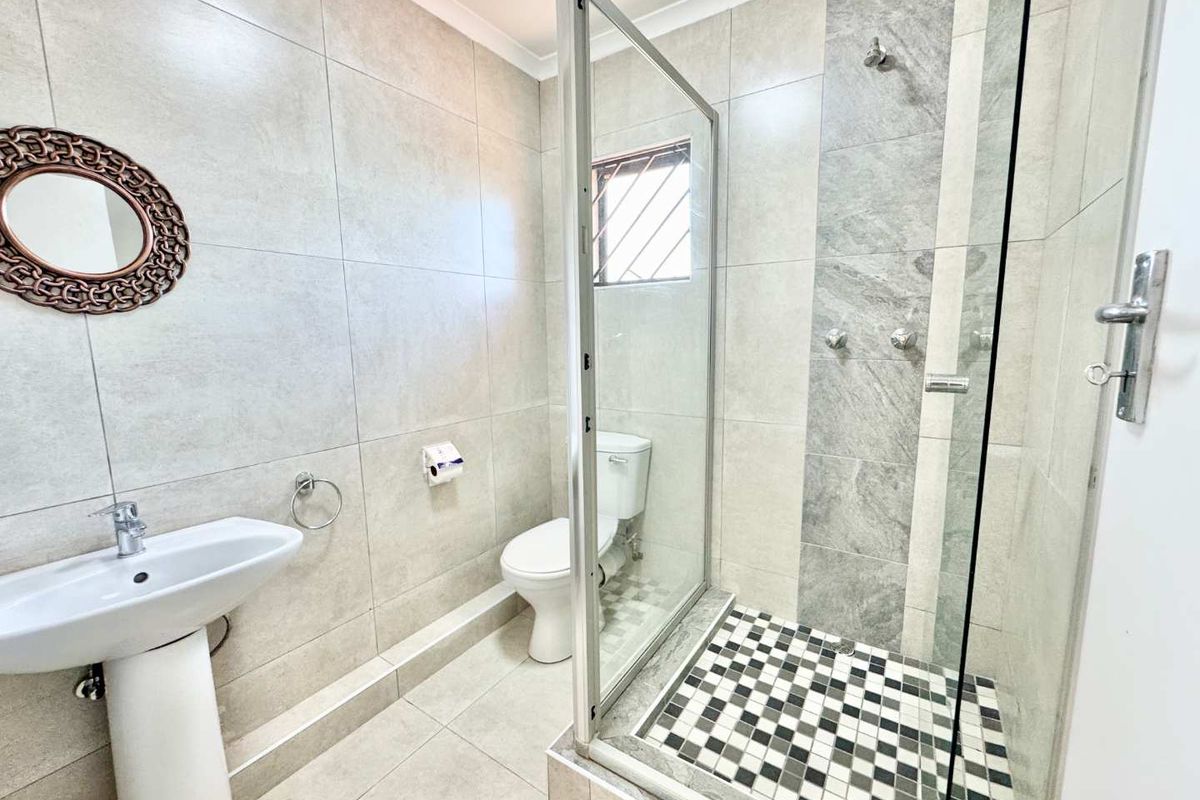 Modern bathroom featuring a glass-enclosed shower with decorative mosaic floor tiles, a pedestal basin, and neutral wall tiling.