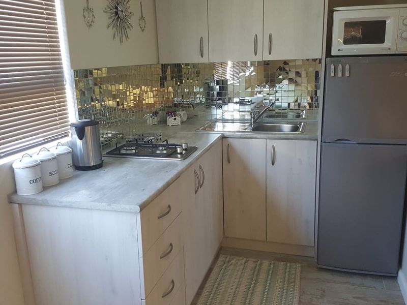 Compact kitchen featuring light-toned cabinetry, laminate countertops, a gas hob, and a distinctive mirrored tile backsplash, providing a functional and efficient cooking space.