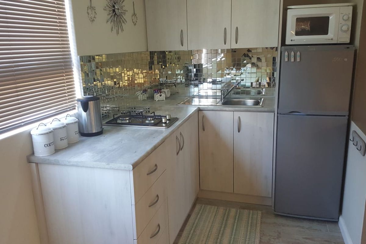 Compact kitchen featuring light-toned cabinetry, laminate countertops, a gas hob, and a distinctive mirrored tile backsplash, providing a functional and efficient cooking space.