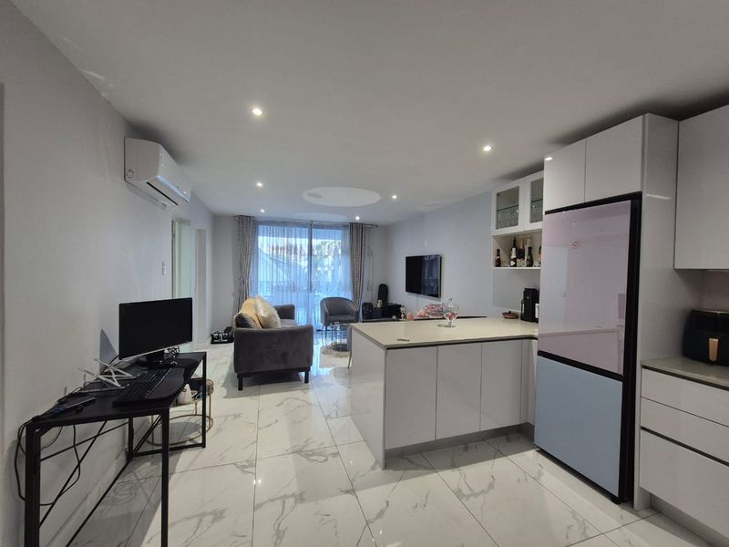 Modern open-plan living area featuring sleek marble-look floor tiles, recessed lighting, a contemporary kitchen island, and direct access to an outdoor space.