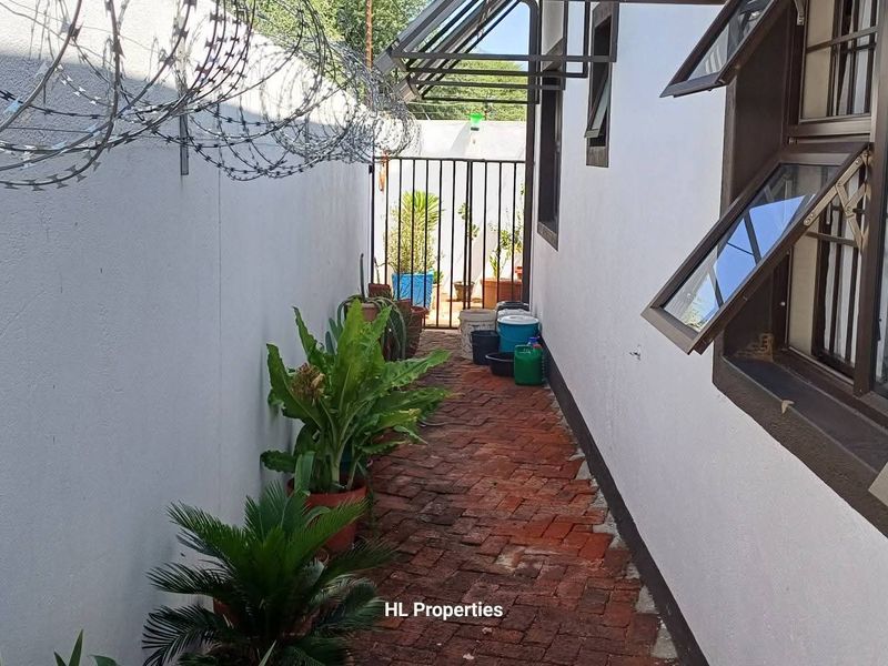 A narrow side passage featuring brick paving, security fencing with razor wire, and metal-framed casement windows.