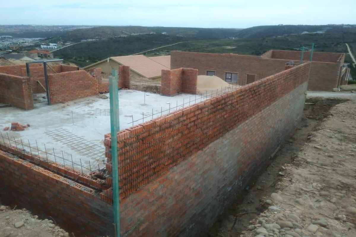 An elevated view of a residential property under construction, featuring exposed brick walls and concrete foundation slabs in a developing estate.