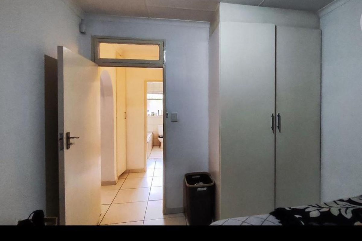 A bedroom featuring built-in cupboards and tiled flooring, with a doorway leading to an adjacent bathroom area.