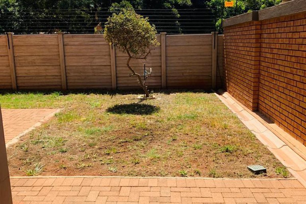 A private rear garden featuring a paved patio area, a small lawn section, and secure perimeter brick and panel fencing.