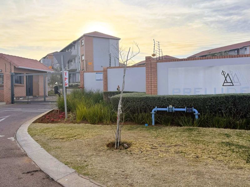 Front entrance view of the apartment complex featuring a secure gated access point, perimeter wall with electric fencing, and landscaped garden area.