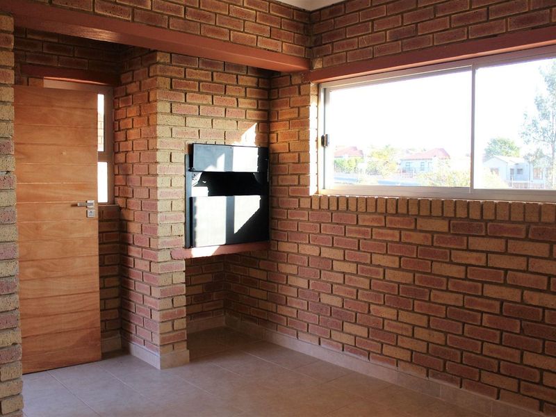 An empty living area featuring exposed brick walls, a built-in fireplace, tiled flooring, and a large sliding window providing natural light.