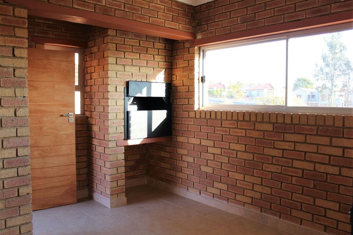 An empty living area featuring exposed brick walls, a built-in fireplace, tiled flooring, and a large sliding window providing natural light.