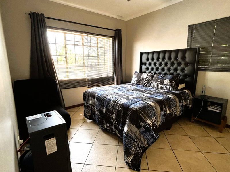 A bedroom featuring tiled flooring, window blinds, and curtain rails, providing a functional space with neutral wall finishes.