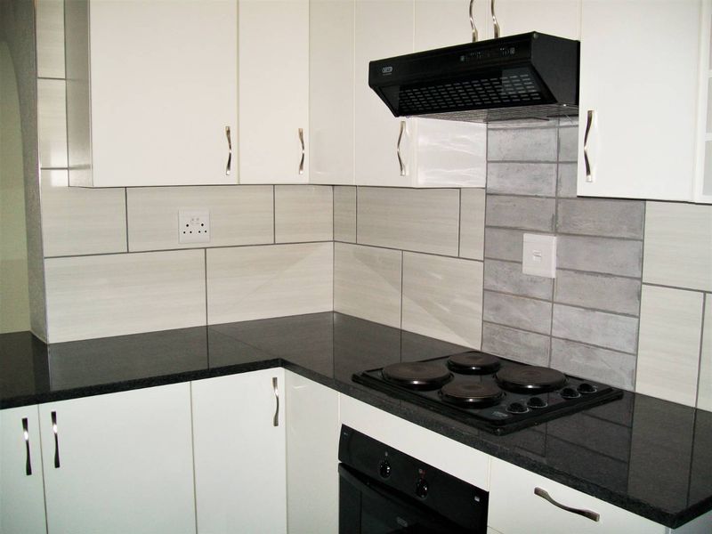 Modern kitchen featuring white cabinetry, dark granite countertops, a built-in oven, electric hob, and a stylish tiled backsplash.